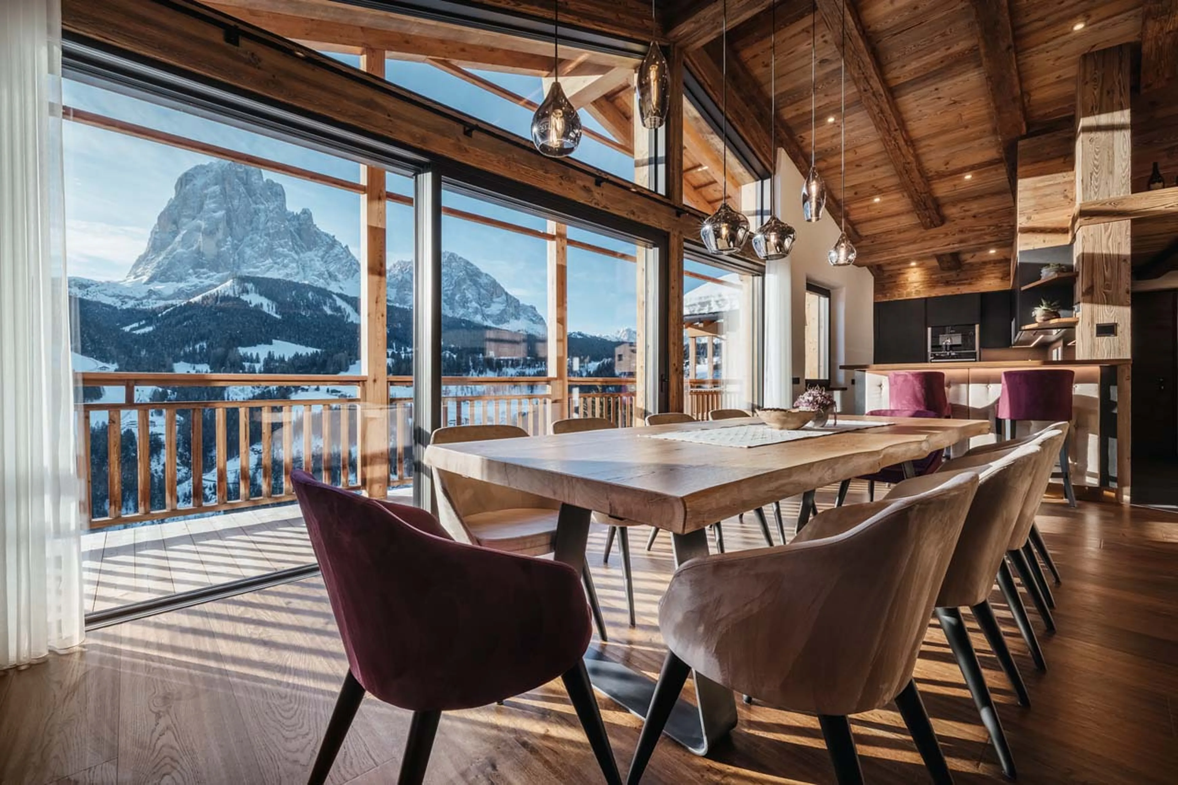 Dining table beneath expansive glass windows in Chalet Lefiro, Val Gardena