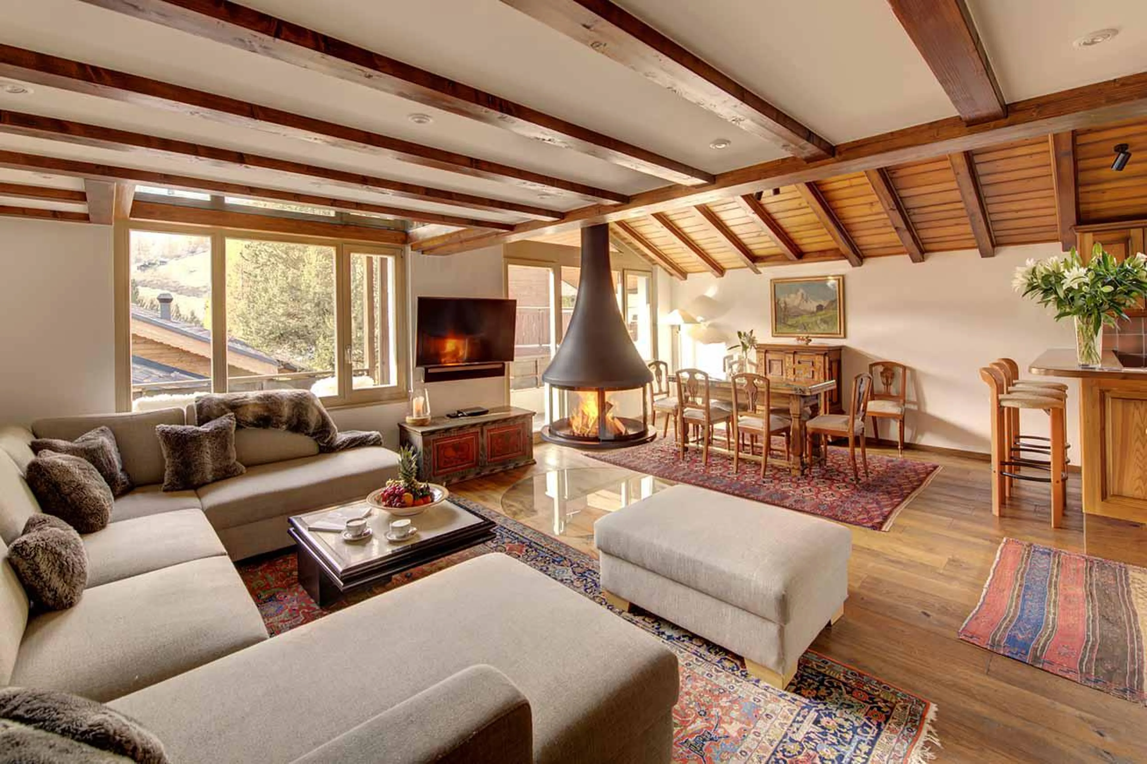 Open-plan living and dining area with central steel hanging fireplace at Penthouse Zen in Zermatt